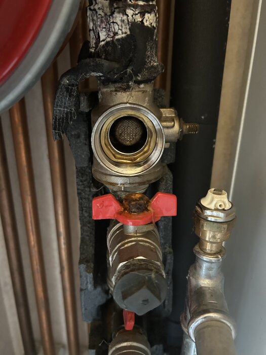 Bergvärmepumpens rördel med exponerat filter, röd ventil på koppling.