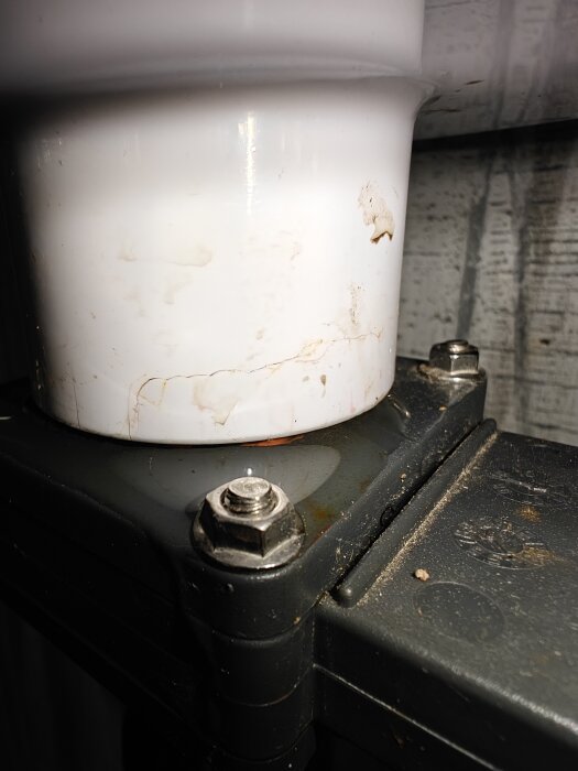 Vit plastledning ansluten till svart metallbeslag, med små läckagespår på ytan.