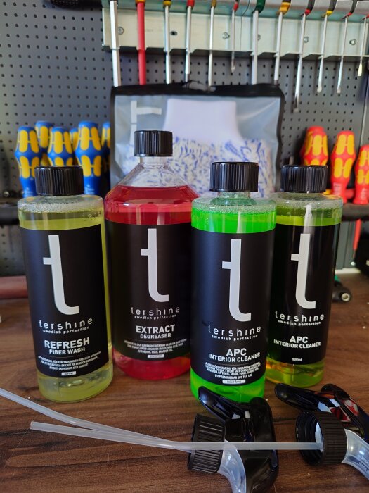 Fyra flaskor Tershine rengöringsprodukter och sprutmunstycken på en verkstadsbänk, med verktyg hängande i bakgrunden.