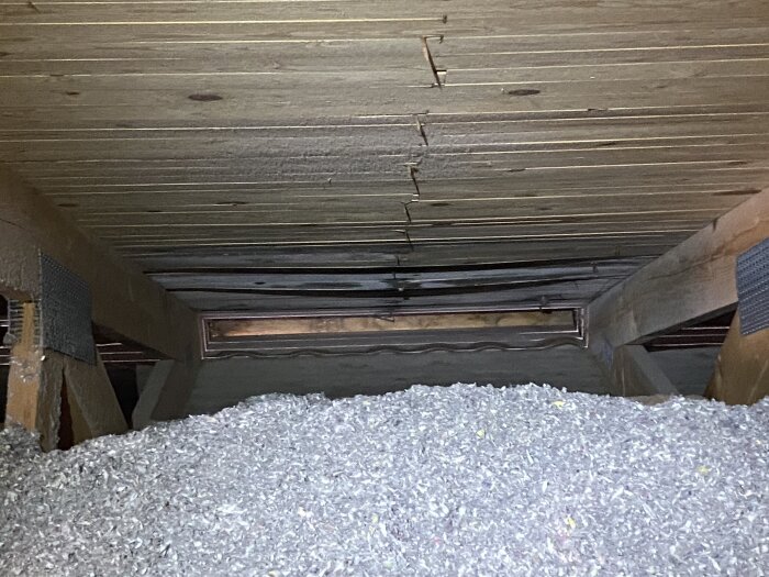 Tilläggsisolerad vind med lösull, synlig råspont ovanför och ventilationsöppning; tecken på fukt och mögel.