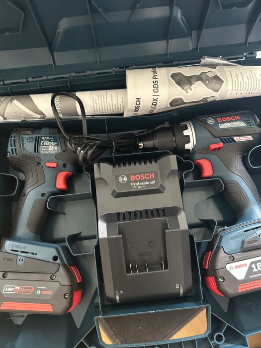 Bosch borrskruvdragare med laddare och batterier i en verktygslåda, inklusive instruktioner.
