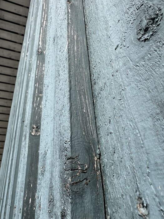 Blåmålad träfasad med torrsprickor närbild, visar ljusa partier och slitet område för bedömning av underhållsbehov.