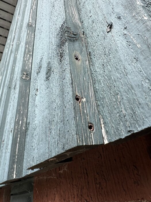 Sliten träfasad med avflagnad färg och torrsprickor. Nagelhuvuden synliga i träet. Diskussion om behov av målning.