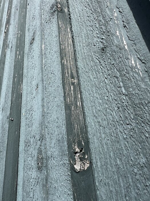 Sliten fasad med torrsprickor i träet, med färg som delvis har flagnat.