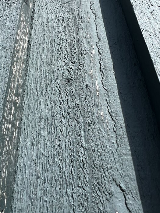 Fasadens träpanel med sliten blå färg och ljusa partier, eventuellt torrsprickor. Fråga om fasadtvätt och målning behövs.