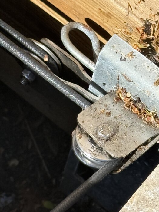 Närbild av en sliten trissa för en linbana, där en kabel löper över metallskivorna, omgivna av smuts och träfragment.