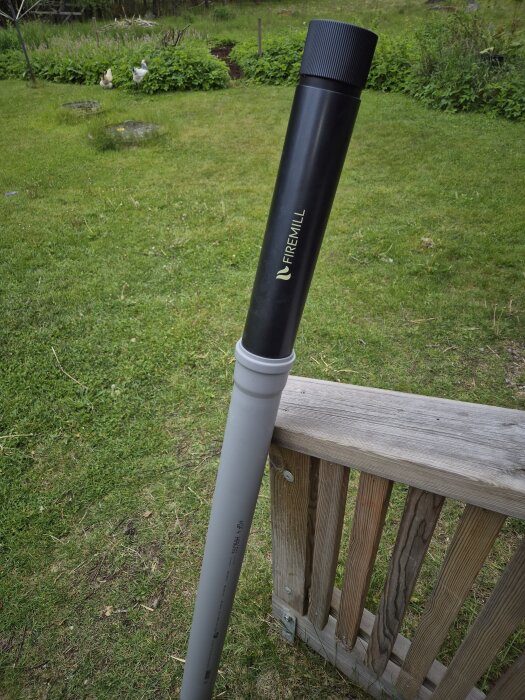 Handsläckare märkt "Firemill" monterad på ett grått avloppsrör, placerad utomhus på gräsmatta intill ett staket.