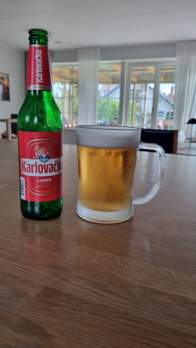 Flaska Karlovacko lager och ölglas på nyslipat och oljat altanbord.