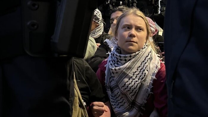 En person med en svartvit mönstrad sjal om halsen sitter omgiven av andra människor under en utomhusprotest.