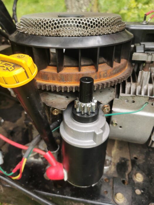 Närbild av en trädgårdstraktors motor från sidan, med fokus på en startmotor och svänghjul med synlig rost.
