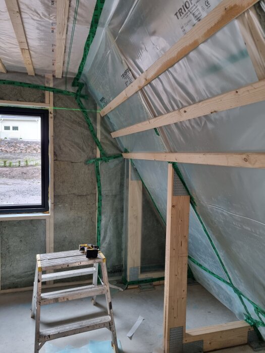 Väggar i konstruktion med plast och träreglar. En stege med verktyg står i rummet nära ett fönster.