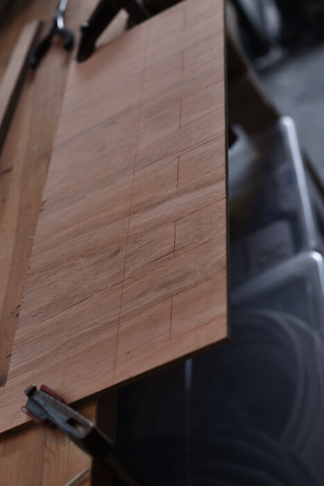 Plywoodskiva med linjer för kapning, del av ett projekt för batterihållare i ett garage.