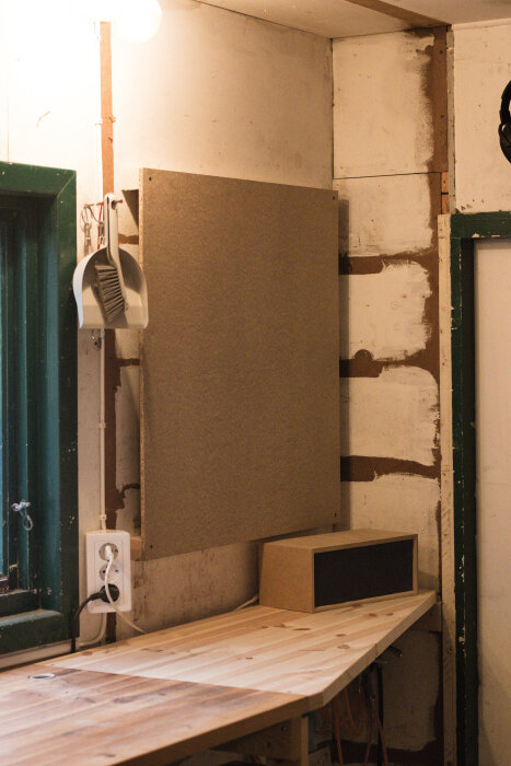 En översikt av en verktygstavla på en vägg med ett anslutet eluttag, en städborste, och en träbänk under.