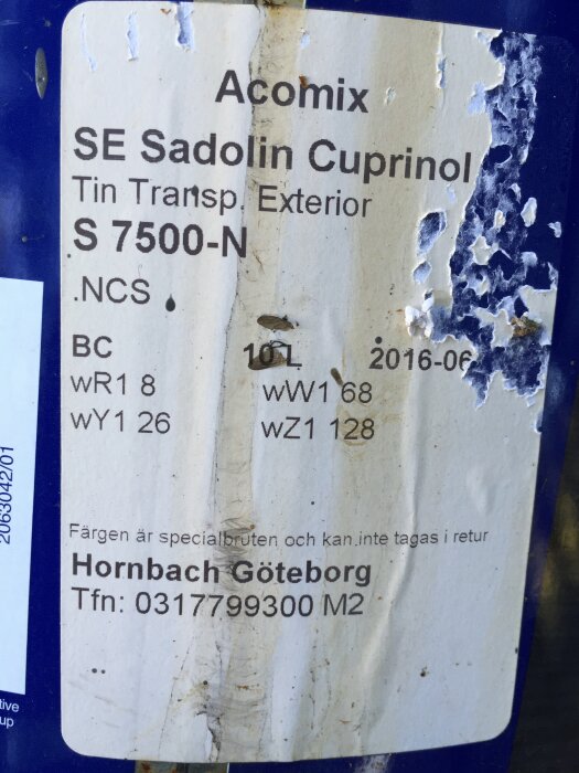 Etikett på burk med täcklasyr; "Acomix SE Sadolin Cuprinol Tin Transp Exterior S 7500-N". Detaljer inkluderar färgbeteckningar och kontaktuppgifter till Hornbach Göteborg.