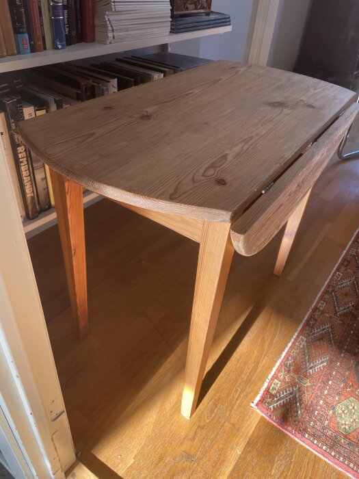 Träbord med en nyligen avskalad yta i ett rum, omgiven av böcker på en hylla. Bordet är utan lack och redo för avlutning.