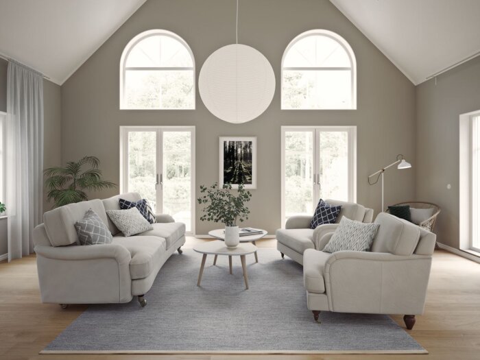 Vardagsrum med takfönster och ljusa soffor, centralt placerat soffbord, rund lampa i taket, samt inredningsdetaljer som kuddar och växter.