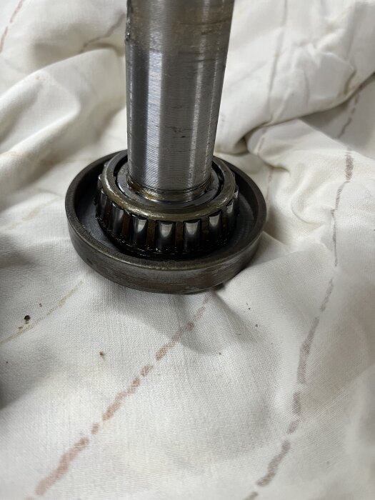 Koniskt kullager utan fett på en metallaxel, placerad på ett ljust tyg.