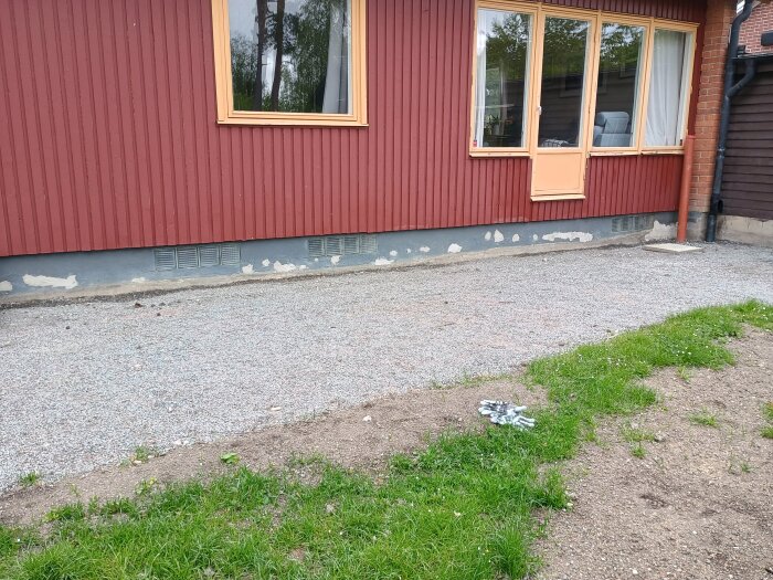 Baksidan av ett hus med grundmålad vägg och fönster, grus och gräs i förgrunden.