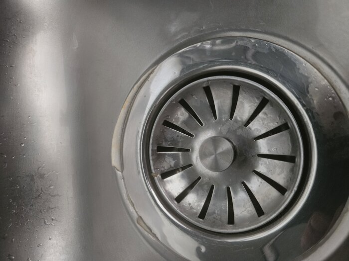 En närbild på en metallisk diskbänksavlopp där en gummipackning sticker upp på ena sidan.