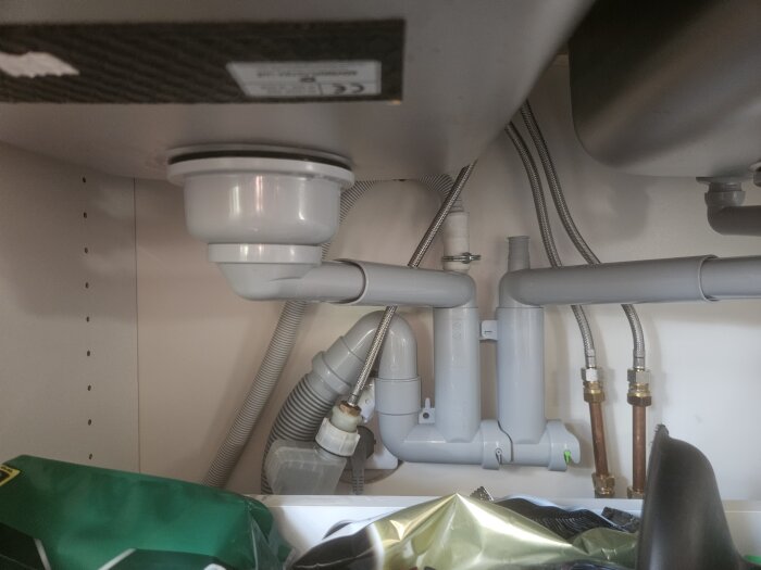 Under diskbänken visas rör och avloppssystem med en lyft packning vid diskhon.
