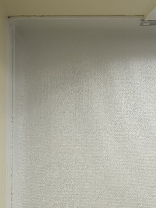 Ett tak med tydlig struktur av glasfiberväv och flera lager färg, med en annan nyans än angränsande rum. Detaljerat och ojämnt.