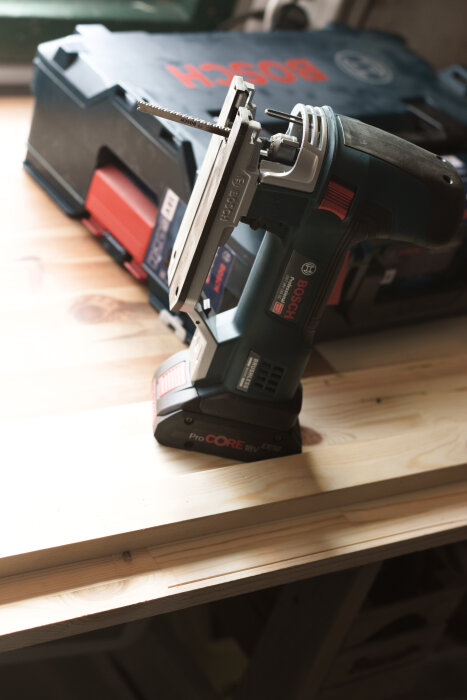 Bosch sticksåg med batteri placerad på träbord nära en Bosch verktygslåda.