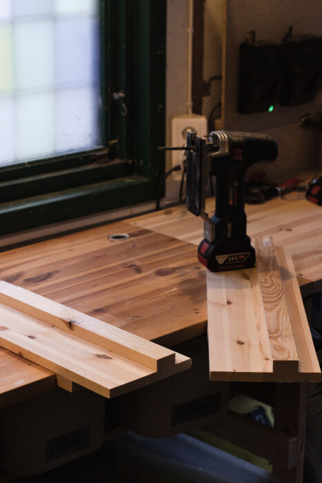 En sticksåg står på ett arbetsbänk av trä bredvid hemmagjorda sågskenor och plankor.