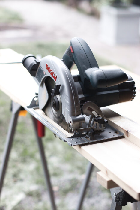 Cirkelsåg av märket Bosch placerad på ett träbord utomhus. Den används i ett projekt för att bygga hemmagjorda sågskenor.