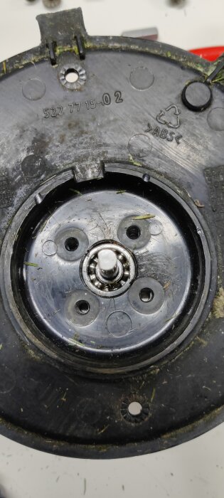Närbild av en svart plastkomponent med synligt kullager, saknar packning eller bussning. Gräsrester finns runt lagret.