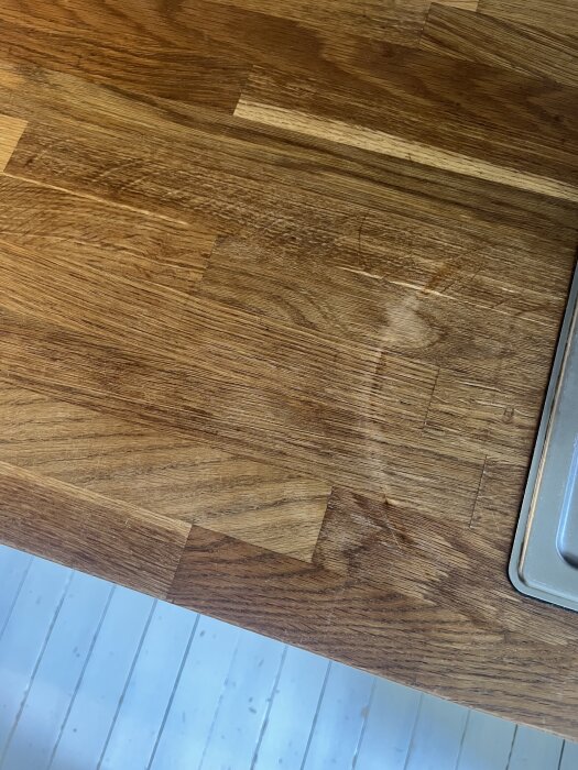 Ljusa fläckar på köksbänkskiva av trä bredvid diskho, resultat av överdrivet gnuggande för att ta bort gjutjärnspanna-fläck.