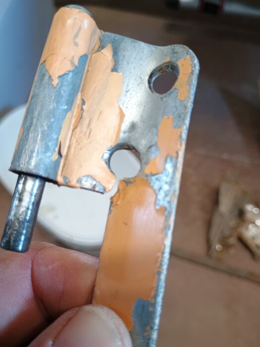 Gångjärn från en altandörr, avskavt och slitet, hålls i en hand.