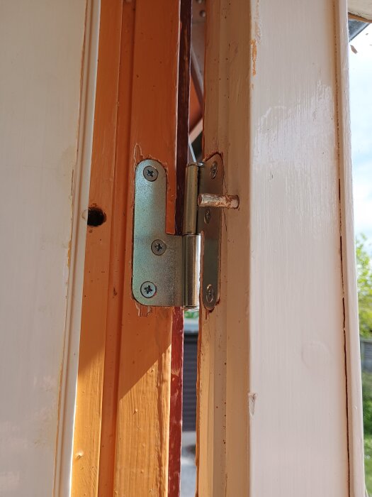 Gångjärnet på en altandörr som har gått sönder, med tecken på slitna fästen i dörrkarmen.