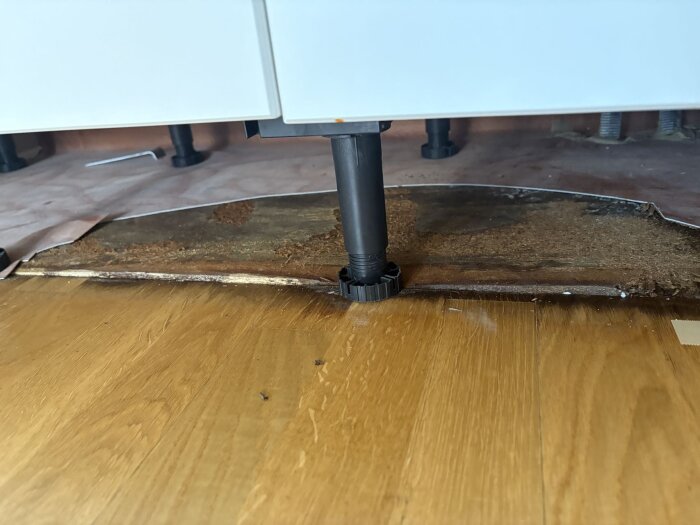 Skadad diskbänksbotten i trä med mörka fläckar orsakade av läckage, delvis borttagen för att visa fuktskador.