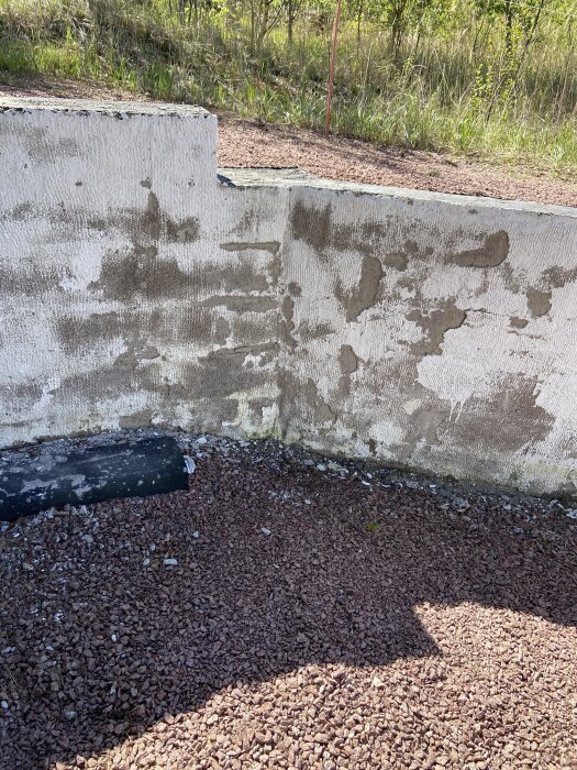 Sliten lättklinkervägg med delvis avflagnad tunnslamning och silikatfärg, samt en Platonmatta vid basen.