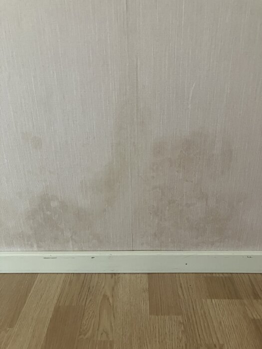 Vägg med otydliga, mörka fläckar ovanför ett trägolv.