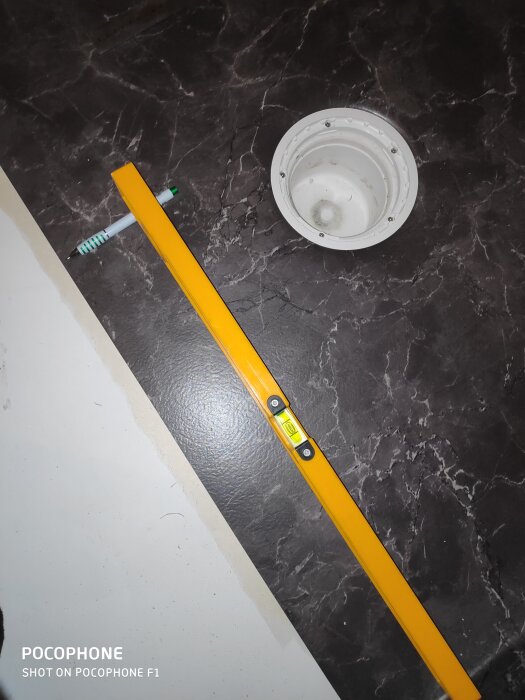 Vattenpass på mörkt badrumsgolv bredvid en rund duschbrunn, visar lutningen i badrumsrenovering.