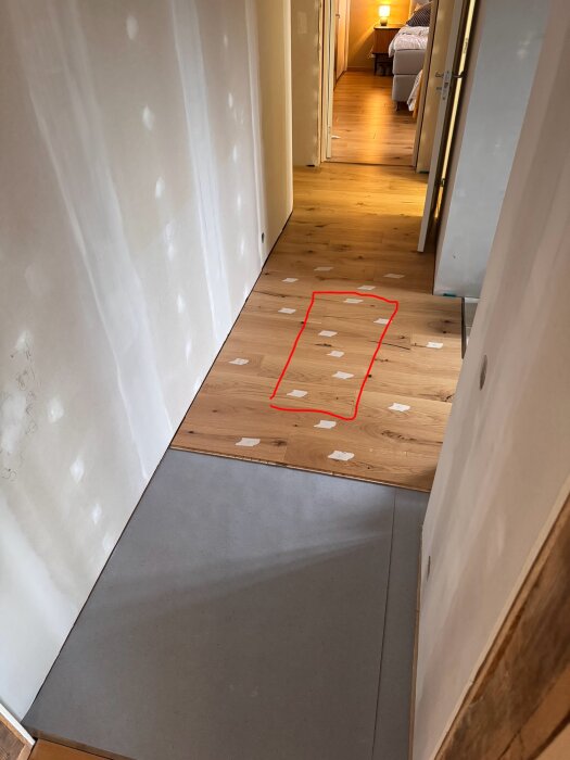 Hall med trägolv och röda markeringar som visar ett påverkat område. Papperslappar är utplacerade på golvet.