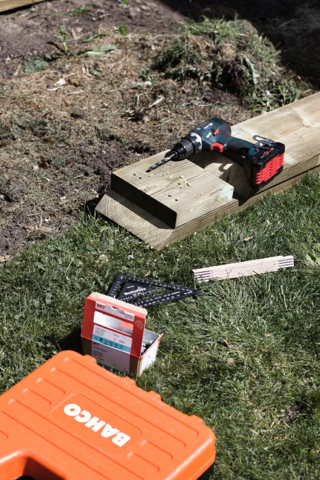 Borrmaskin och verktyg på gräsmatta vid bygget av en odlingslåda.