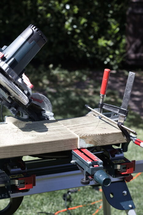 Kap- och gersåg används för att gera hörn på träplank i solljus, fastspända med tvingar på ett sågbord i trädgården.