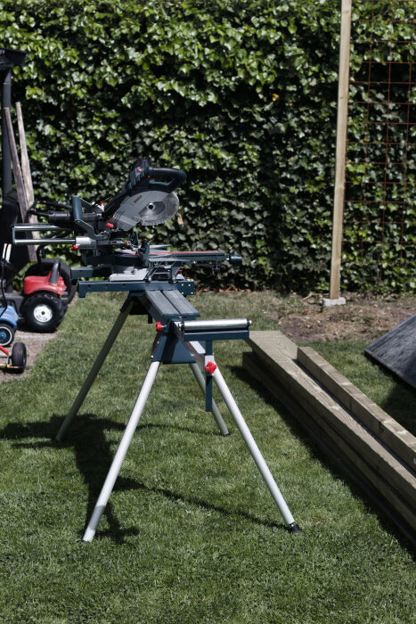 Kap- och gersåg på ett ställ i en trädgård, med träreglar och en spaljé i bakgrunden.