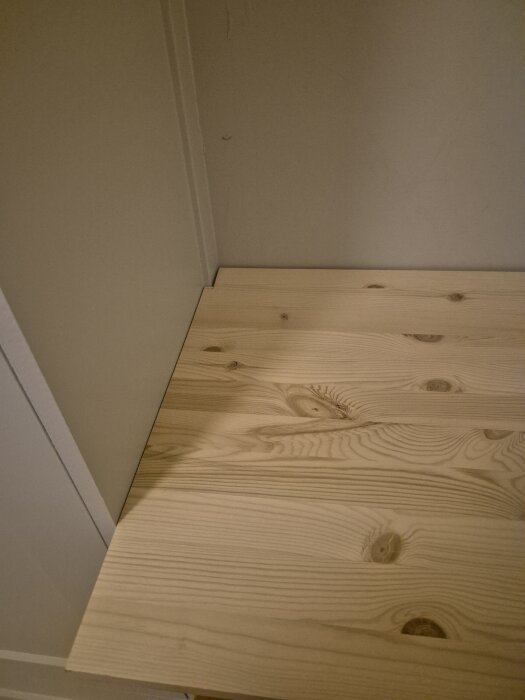 Skrivbordsskiva i trä monterad mot en sned vägg och garderob, med synlig springa runt om.