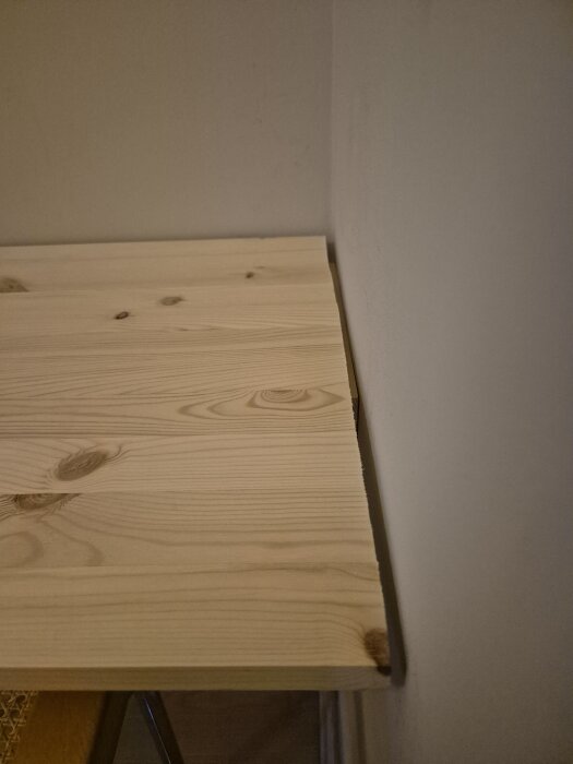 Sned skiva av furu fäst mot en vägg och garderob, med en synlig glipa mellan skivan och väggen på grund av den sneda vinkeln.