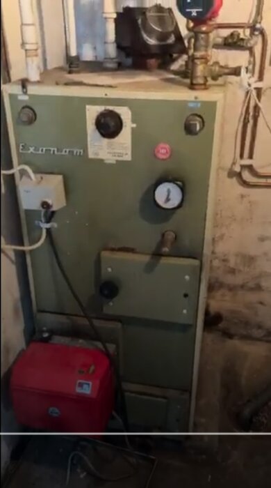 Gammal Exonom oljepanna med mätare och kopparledningar i ett hus, del av diskussion om byte till modernare värmesystem.