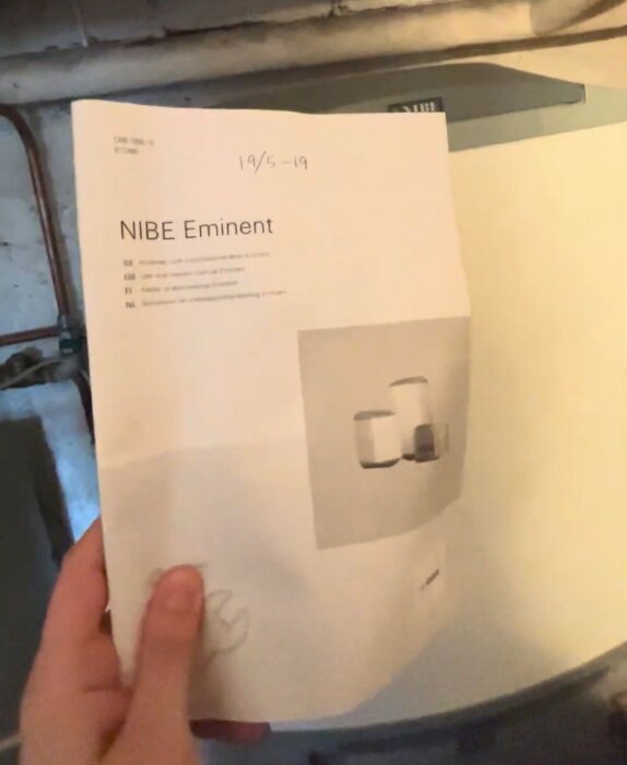 Hand holding a manual for a NIBE Eminent water heater in a discussion about upgrading a home's heating system for winter.