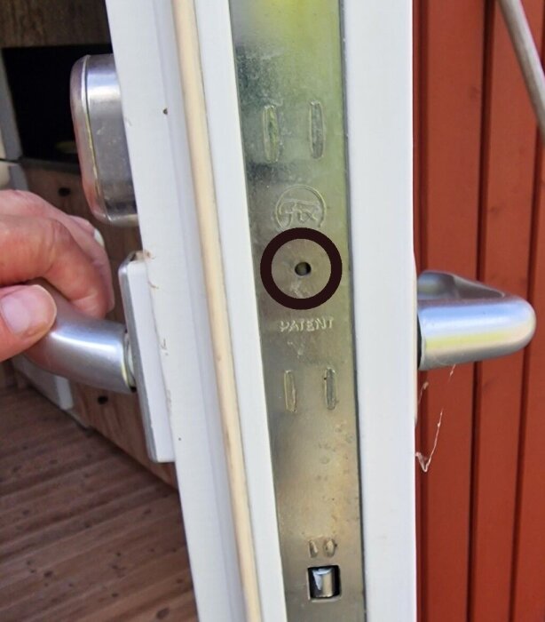 Spanjolett på en dörr med markerat hål för smörjning och en hand som håller i dörrhandtaget.