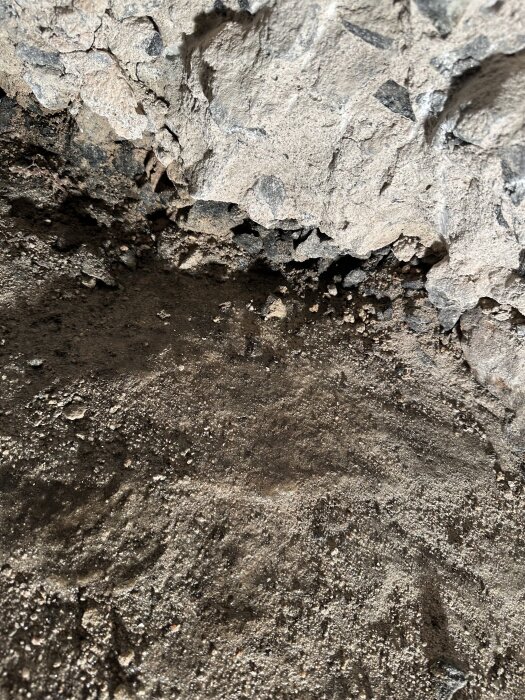 Grundmur och klippt berg i en källare med fukt på golver, tydligt spår av vatteninträngning vid berg och murkontakt.