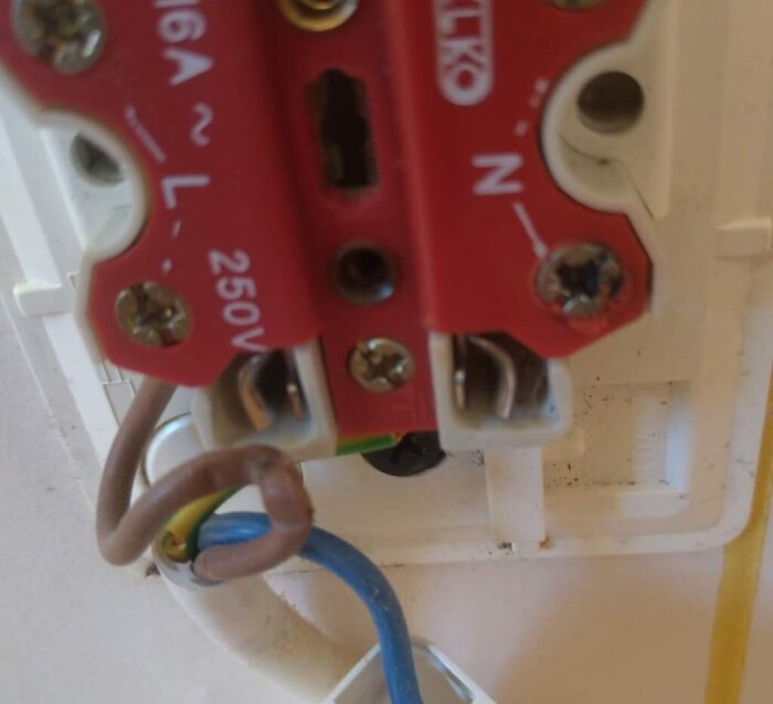 Elektriskt uttag med felmonterade kablar. Blå nolla lös och fasledare klämd, tecken på överhettning och smält plast syns.