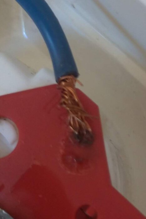 Kabeländar klämda under ett uttagslock med tecken på värmeskador och smält plast.