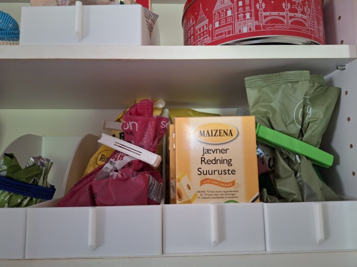 Förvaringslådor i köksskåp med påsar och en Maizena-förpackning, skapar ordning för matvaror.