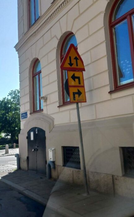 Vägskyltar vid ett gathörn visar både mötande trafik och vänstersväng samt högersväng på en gul bakgrund.
